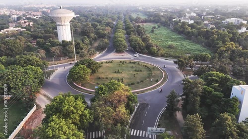 Aerial video of a landscaped roundabout in Greater Noida, where tree-lined roads intersect around a circular green island, highlighting planned infrastructure and smooth urban traffic flow.