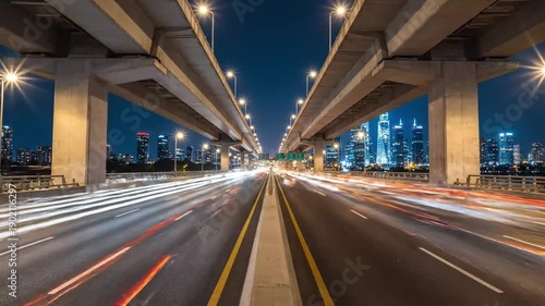 Dynamic nighttime cityscape view with light trails on a highway overpass showcasing modern urban infrastructure and fast-paced movement against a vibrant skyline