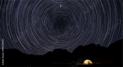 Lone campsite under a swirling sky of star trails and mountains