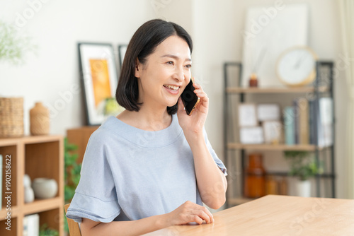 Foto リビングでスマホで電話をするミドルの女性