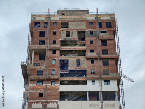 Quadro su tela Solitary brick tower in progress alongside crane against distant cityscape obser