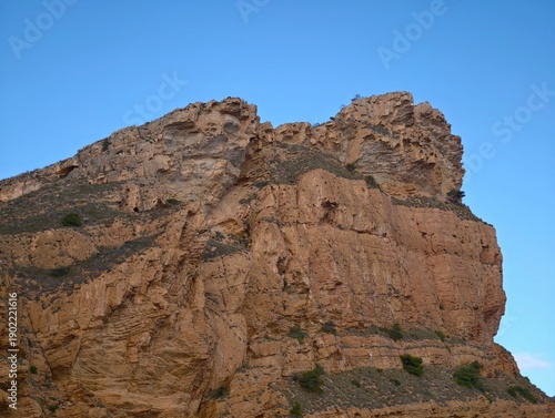Schilderij op canvas Skyward rock face with shadows, Imposing rocky precipice against azure sky with