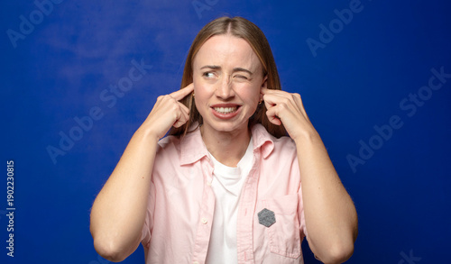 Fotografía looking angry, stressed and annoyed, covering both ears to a deafening noise, so