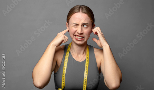 looking angry, stressed and annoyed, covering both ears to a deafening noise, sound or loud music. fitness concept