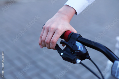 Close up of a hand gripping a bikes brake lever with red grip, sharp focus on fingers and mechanism, blurred pavement background suggests motion readiness.