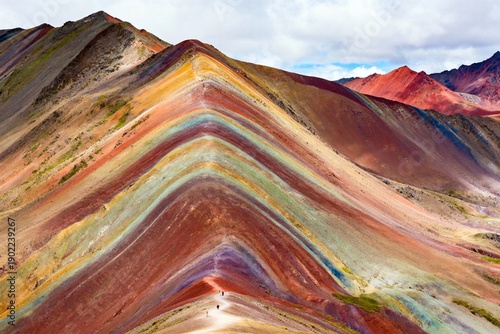 Vividly colored stratified mountains with layered earth tones under a partly cloudy sky