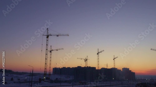 4k timelapse with vibrant winter sunrise over a massive urban construction site, featuring multiple tower cranes and new residential buildings under development in the snow.