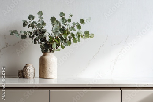 Eucalyptus arrangement in a beige vase on a bright countertop with small decorative vases