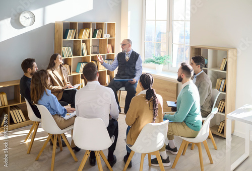 Group students and professor in library seminar. Seated in a circle, they listen and exchange ideas. Ideal for education, coaching and training. Clear mentoring and leadership concept.