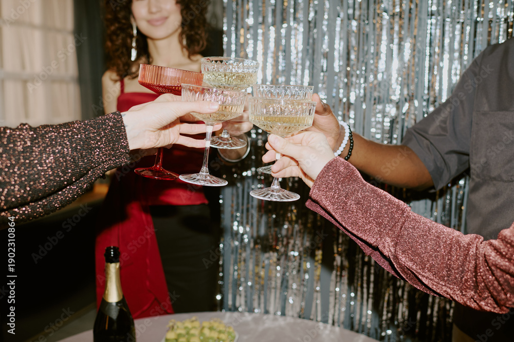 Fototapeta premium Group of young adult and middle aged multiethnic men and women clinking champagne glasses during celebration, hands holding drinks in foreground, smiling woman in background