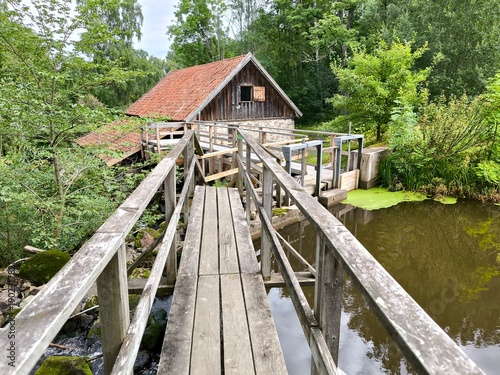 Rasmus Kvarn, Sweden - August 30th 2024: View of Rasmus Kvarn, a traditional wooden water mill with a red tiled roof, wooden footbridge and surrounding forest landscape in Sweden