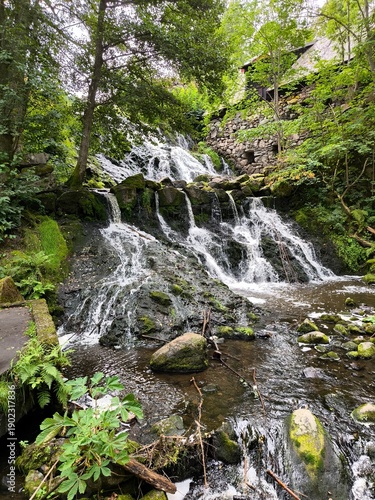 Rasmus Kvarn, Sweden - August 30th 2024: View of Rasmus Kvarn, a traditional wooden water mill with a red tiled roof, wooden footbridge and surrounding forest landscape in Sweden