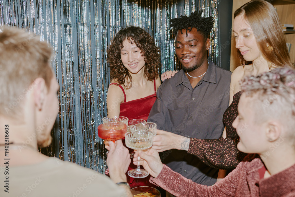 Fototapeta premium Group of young adult multiethnic friends celebrating together, standing close and clinking cocktail glasses, smiling and enjoying festive moment at party with shimmering backdrop