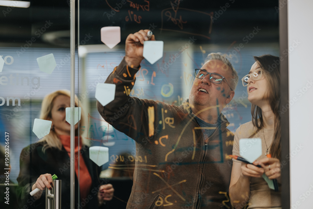 Fototapeta premium A group of professionals brainstorm at a glass wall covered with sticky notes and diagrams. They collaborate to plan ideas and drive a project forward in a modern office.