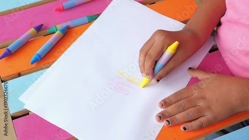 Child draws with crayons on colorful table