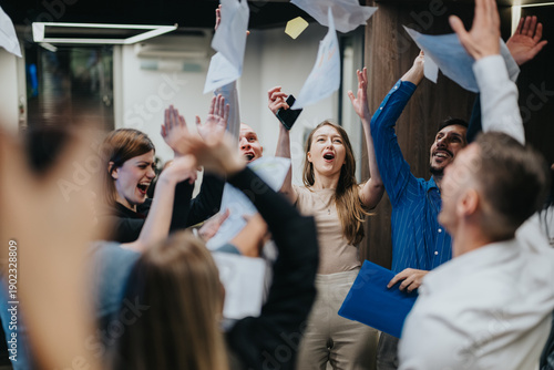 Tableau sur toile A diverse team of coworkers cheers, raises hands, and tosses papers in a lively office celebration