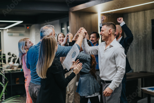 Foto A group of colleagues cheer and high-five to celebrate a win in an office