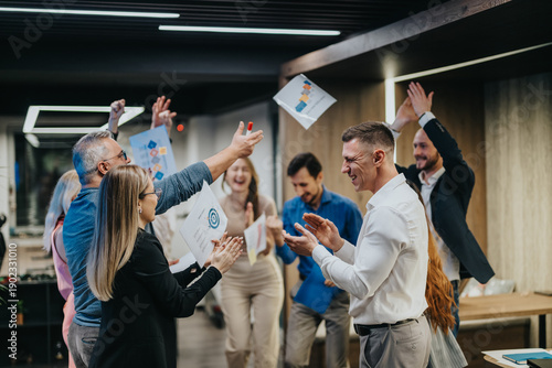 Photography A group of coworkers celebrates a project win, tossing papers and clapping