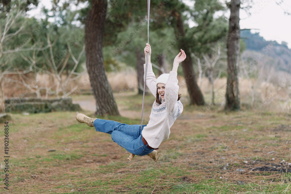 Naklejka premium Woman on a swing in an outdoor park, carefree moment, smiling and enjoying fresh air, nature around, casual outfit, playful balance, rustic setting, serene afternoon, light breeze, candid lifestyle