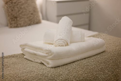 Three white towels are stacked on top of each other on a bed