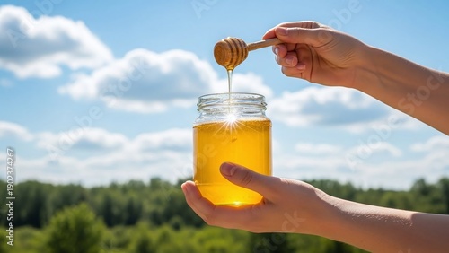 Hands delicately hold a clear glass jar of golden honey, with a wooden dipper dripping liquid.