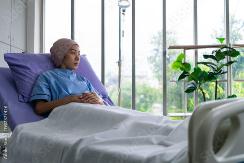 фотографія Asian woman cancer patient sitting alone on a hospital bed receiving saline and looking outside window in hospital ward with feeling of stress and lonely