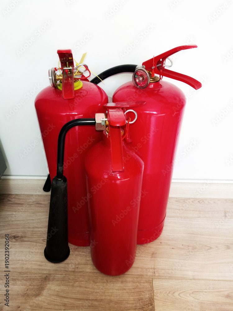 Obraz premium Red fire extinguishers standing on a floor against a white wall for safety compliance