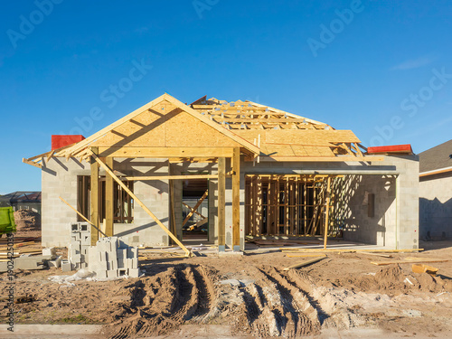 Concrete shell of a one-story single-family house under construction, with framework roof in progress, in a suburban residential development on a sunny day in southwest Florida. Street view.