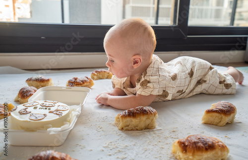 A baby is laying on the floor next to a box of donuts