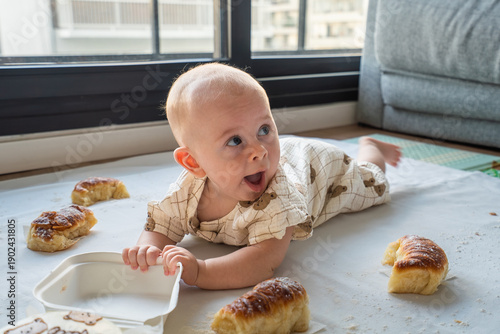 A baby is laying on the floor next to a box of donuts