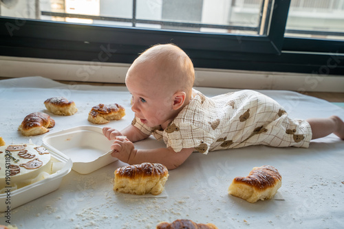 A baby is laying on the floor next to a box of donuts