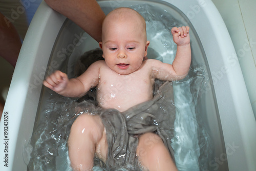 A baby is in a bathtub with water splashing around him