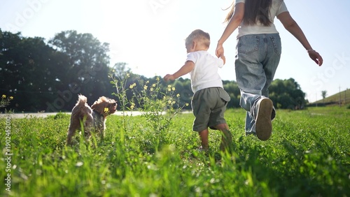 Woman, child and dog enjoying jogging in park. Child holding woman's hand while dog running ahead. Peaceful family moment in nature concept
