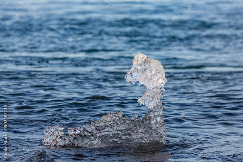 Shimmering ice fragments drift along the shore of Diamond Beach near Jökulsárlón glacier lake as soft afternoon light glows across Southern Iceland’s quiet waves and distant volcanic coastline