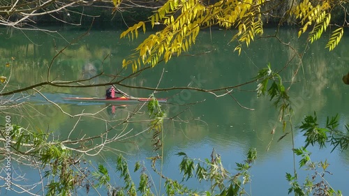 Turin, Italy. Peaceful view of the Po River in Turin with two elderly people canoeing on calm water, framed by autumn leaves, capturing active lifestyle, nature and serene city river mood.