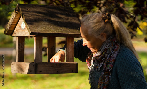 Φωτογραφία A beautiful old lady cares about the birdhouse and birds in a park