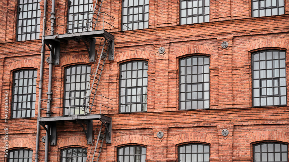 Obraz premium Industrial red brick building facade with repetitive windows, urban architecture background for design, construction and renovation concepts.