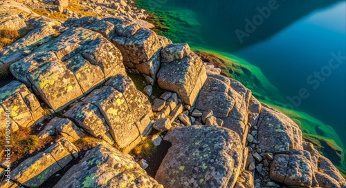 Stunning aerial view of sun-drenched rocky terrain overlooking a crystal-clear turquoise lake