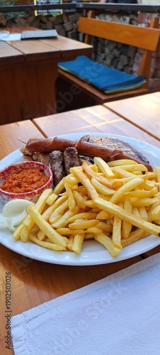 Crispy golden French fries as the main focus of the dish, served on a plate with juicy steak and grilled sausages. The sauce is placed directly on the plate in a small separate dipping bowl