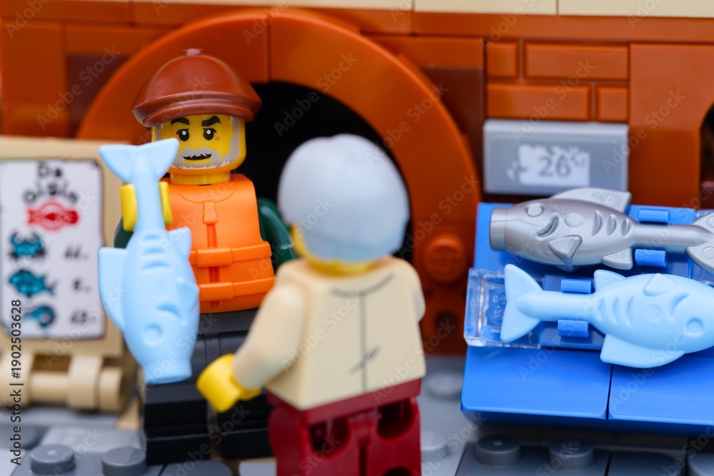 Fototapeta premium Tambov, Russian Federation - January 19, 2026 Close-up shot of a Lego fisherman minifigure selling a light blue fish from a fish stall to a customer.