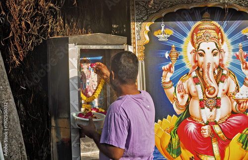 Billede på lærred A person stands before a small outdoor shrine in Penang, placing offerings with