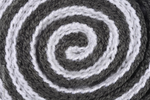 Close up view of a soft wool knitted scarf rolled into a spiral shape showing alternating grey and white circular patterns with visible yarn texture