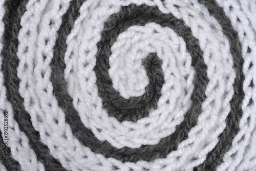 Close up view of a handmade knitted fabric rolled into a spiral shape featuring alternating white and grey yarn with a soft woolen texture