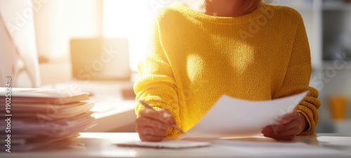 The woman in a yellow sweater reviewing documents at a sunlit desk