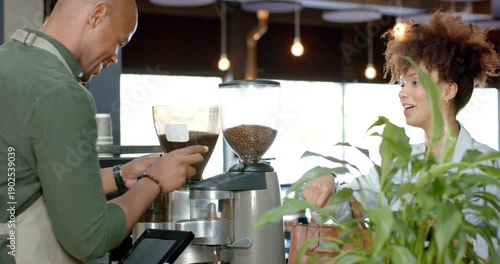 Customer is tapping wrist at service counter, barista is adjusting grinder and preparing espresso