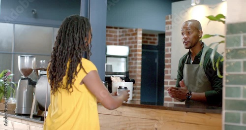 African American customer in yellow approaching counter taking cup for pickup as barista brewing