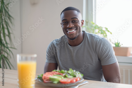 Wallpaper Mural A handsome, smiling Black man sits at a table near a bright window, with a healthy salad and orange juice. Copy space. Joyful lifestyle, fitness nutrition, morning routine concept. Torontodigital.ca