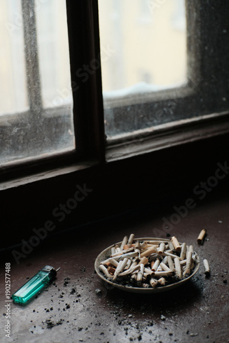 Wallpaper Mural Ashtray filled with cigarette butts on a dusty window sill. Dark moody lighting illustrating addiction, bad habits, and loneliness. Torontodigital.ca