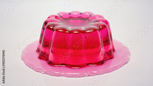 Colorful pink jelly dessert in a vintage mold, placed on a white surface. Soft light highlights the transparent texture and glossy finish of the gelatin.