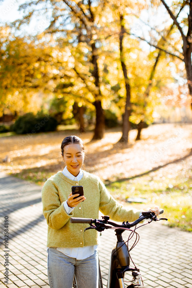 © BGStock72 - Korean woman enjoys a sunny autumn day while texting near her bike in a park